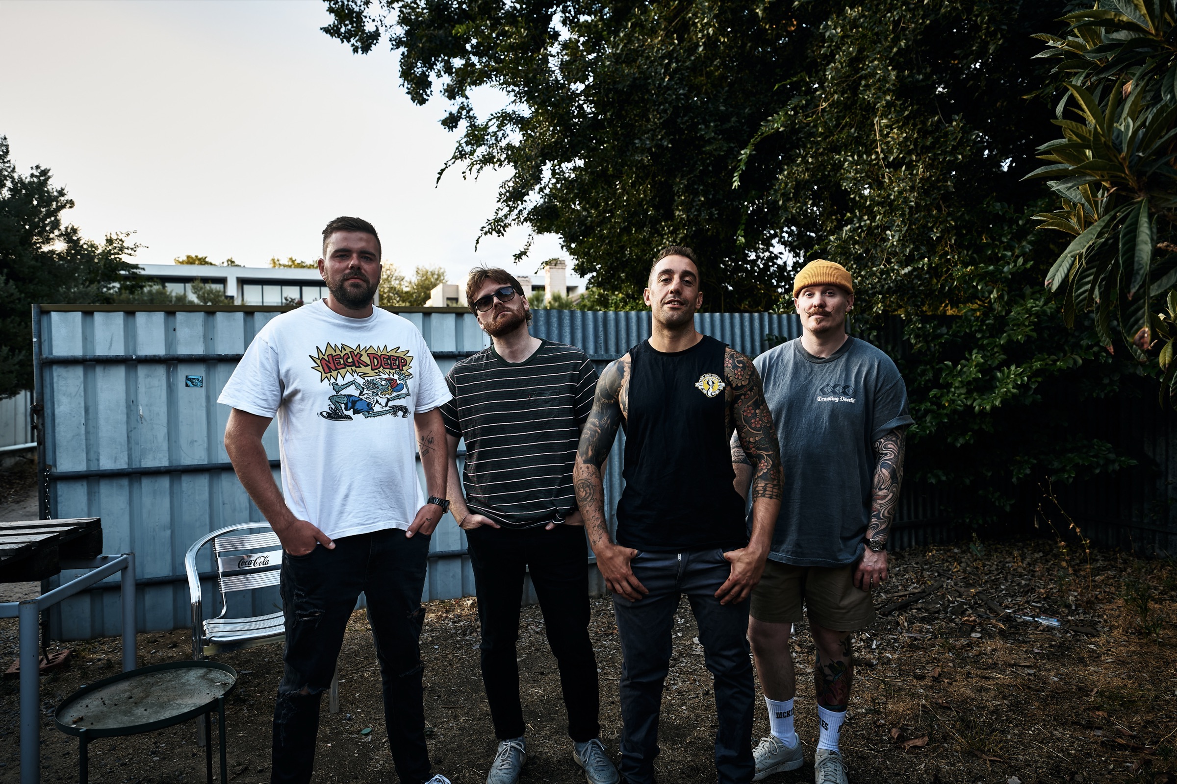 The four members of All Downhill From Here standing in front of a corrugated fence at dusk